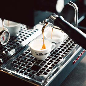 A close-up of a espresso machine dispensing coffee into a white cup, with another cup visible in the background.