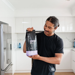 A man in a kitchen holding a bag of Easy Street by Dimattina Coffee