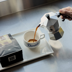Person pouring coffee from a Moka pot into a Dimattina cup