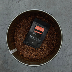 A bag of Mr. Dynamite coffee placed in a tin of coffee beans
