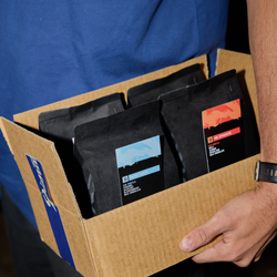 A person in a blue shirt holds a cardboard box containing the Dimattina Blend Trial Pack