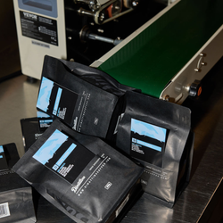 Bags of Prima Tazza piled up next to a bag sealing machine